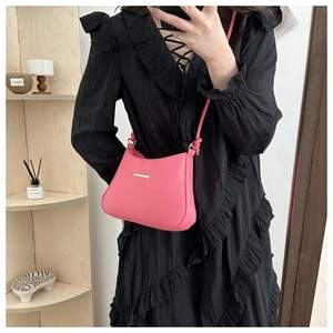 Detail view of a bright pink crossbody bag with gold metal trim worn over a black dress