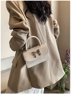 Detailed shot of white faux leather crossbody bag with elegant metal bow decoration