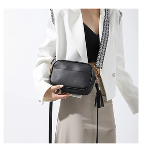 Close-up of black pebble leather crossbody bag with jacquard strap and tassel detail