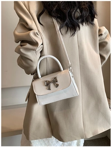 Close-up of cream mini bag with silver bow accent worn as a crossbody by a model