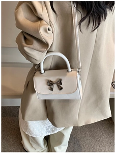 Detail showing white PU leather handbag with silver metallic bow and textured flap