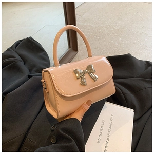 Detail of pink patent leather handbag with polished metal bow and sleek handle