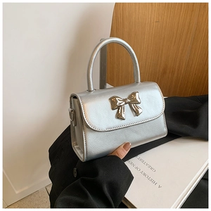 Close-up of silver textured crossbody bag featuring a metallic bow and hard handle