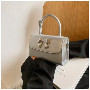 Detail of silver metallic handbag with metal bow accent and sleek circular top handle