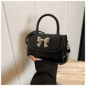 Close-up of black patent leather crossbody bag with silver metal bow hardware