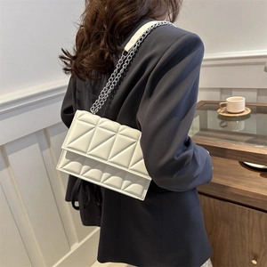 Classic white quilted crossbody bag with silver chain strap worn by model in gray blazer