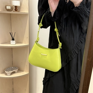 Lime green minimalist crossbody bag with knotted strap and gold accent in home setting