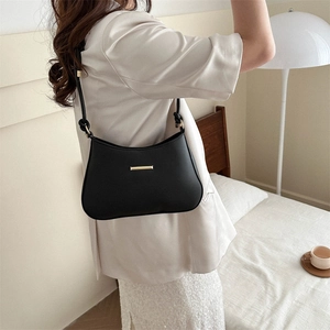 Minimalist black leather underarm bag with gold metal trim shown on model