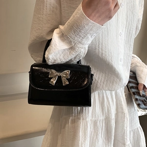 Glossy black leather handbag with silver bow detail worn with white dress