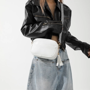 Borsa a tracolla bianca minimalista con cinturino a motivi e nappa in pelle su un modello