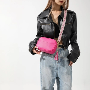 Sac bandoulière en cuir magenta avec pompon et large sangle à motifs sur mannequin