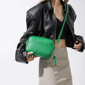 Sac bandoulière vert en cuir avec pompon porté par un mannequin en studio photo
