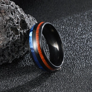 Polished black titanium men's ring with blue inlay and koa wood texture on volcanic rock