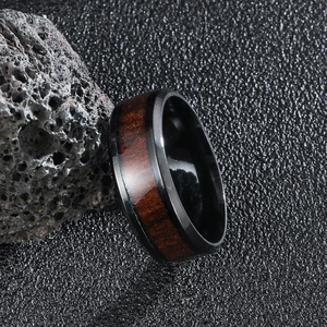 Men's black stainless steel ring with natural wood inlay on dark volcanic rock background