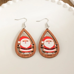 Hölzerne Tropfenohrringe mit Weihnachtsmann-Muster auf einem weißen Keramikteller