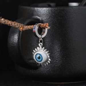 Macro shot of a silver evil eye earring with blue iris hanging on a withered wood branch