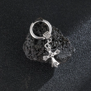 Close-up of vintage titanium steel cross earring on dark volcanic rock background