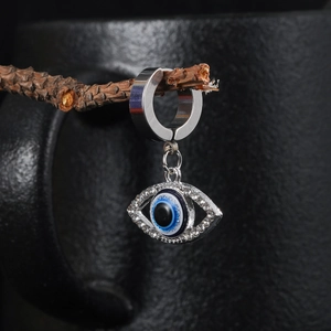 Macro shot of stainless steel Evil Eye earring with blue crystal on a rustic branch