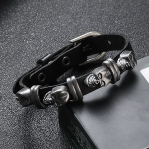 Close-up of punk black leather bracelet with three vintage silver skull metal charms