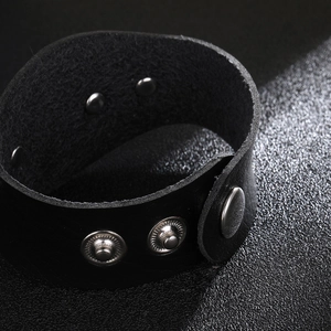 Breites schwarzes Punk-Lederarmband mit drei silbernen Metalldruckknöpfen auf dunklem Grund