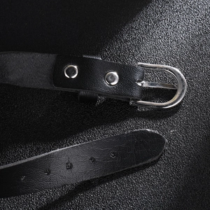 Détail d'une ceinture en cuir noir avec boucle ardillon argentée et rivets sur fond noir