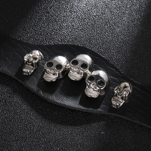 Makro-Detail von fünf silbernen Totenkopf-Nieten auf schwarzem Lederarmband mit Narbung
