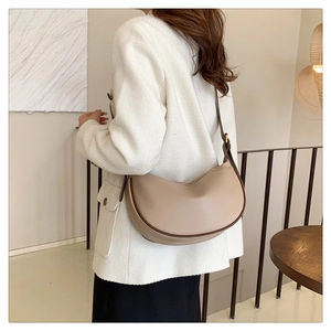 Detail view of a beige crescent moon bag worn by a model in a minimalist room