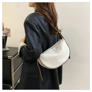Model wearing a white half-moon shoulder bag with brown leather trim in an office setting