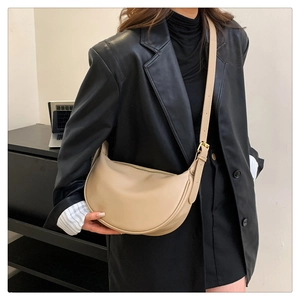 Beige half-moon leather crossbody bag shown on a model wearing a black leather blazer