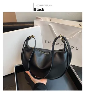 Detail of black crescent shoulder bag leaning on a white gift box with gold metal zipper