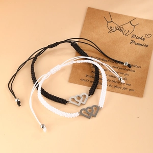 Handmade woven couple bracelets with interlocking silver hearts on a promise card