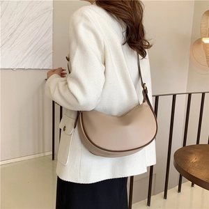 Minimalist beige crescent shoulder bag with dark edge detailing shown on a model