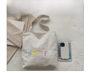 Canvas tote bag with STUFF embroidery shown next to a tablet and phone for size comparison