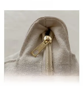 Detailed close-up of smooth gold metal zipper on minimalist canvas tote bag