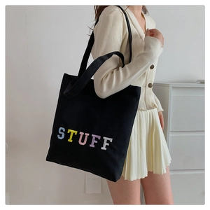 Detail of black canvas tote bag with colorful STUFF embroidery and wide shoulder strap