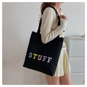 Detail shot of black canvas tote bag featuring colorful STUFF letter embroidery decor