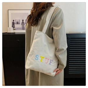 Close-up of white canvas tote bag with colorful STUFF embroidery on a fashion model