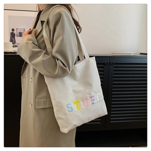 Detailed shot of multicolor STUFF embroidery on a white canvas tote bag with shoulder strap