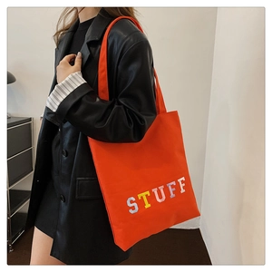 Close-up of bright orange tote bag with STUFF embroidery and wide shoulder strap