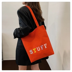Detail of orange canvas tote bag featuring vibrant colorful STUFF letter embroidery