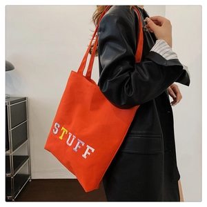 Detail of orange canvas tote bag with 3D colorful 'STUFF' embroidery and black leather jacket