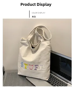 Detail of off-white canvas tote bag featuring colorful STUFF embroidery and handle texture
