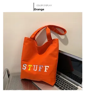 Detailed view of an orange canvas tote bag with colorful STUFF embroidery and wide straps