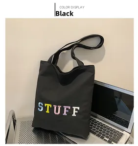 Close-up of black canvas tote bag featuring colorful STUFF embroidery and long handle