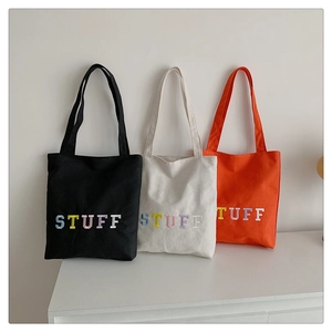 Three canvas tote bags in white, black, and orange featuring colorful STUFF embroidery