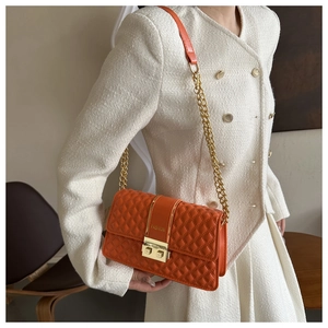 Detail van oranje gewatteerde crossbodytas met gouden ketting gedragen door model