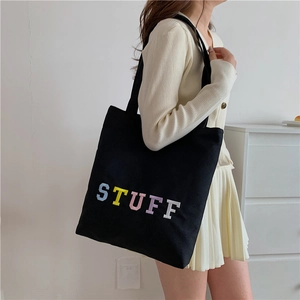 Black canvas tote bag with colorful STUFF embroidery shown on a female model shoulder