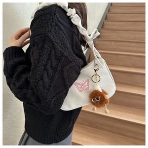 Close-up of white shoulder bag with pink butterfly embroidery and fluffy monster charm
