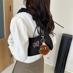 Black underarm bag with pink butterfly embroidery and a plush doll pendant detail