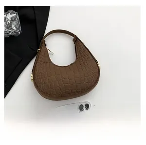 Détail de la texture crocodile marron et de la fermeture éclair dorée du sac sous le bras